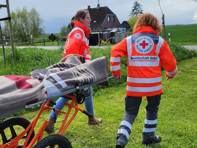 4 Helfer schieben einen Patienten auf unwegsamen Gelände