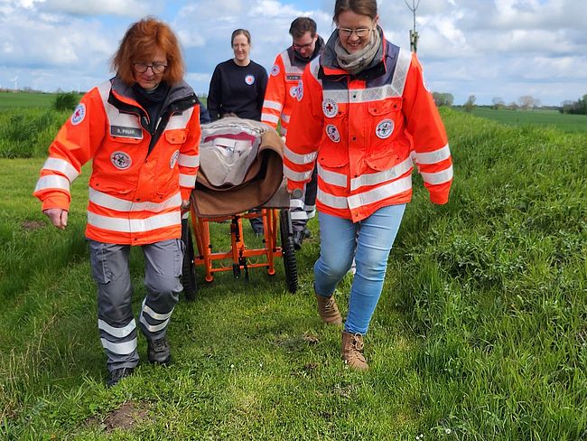 4 Helfer schieben einen Patienten auf unwegsamen Gelände